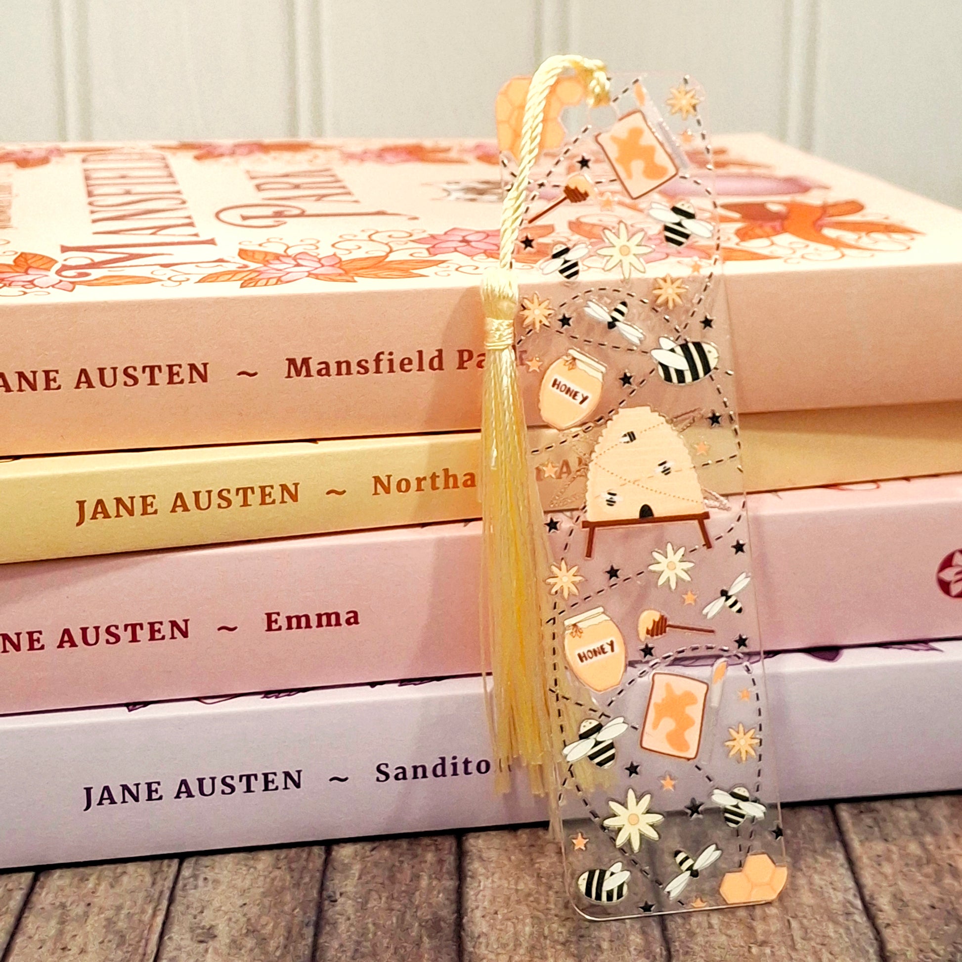 Cute bee themed acrylic bookmark with tassel resting against a stack of books.