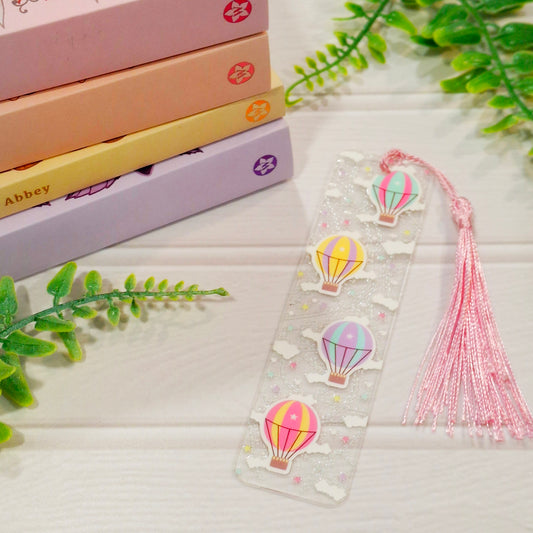 Hot air balloon acrylic bookmark with tassel on a light surface, with books and green leaves.