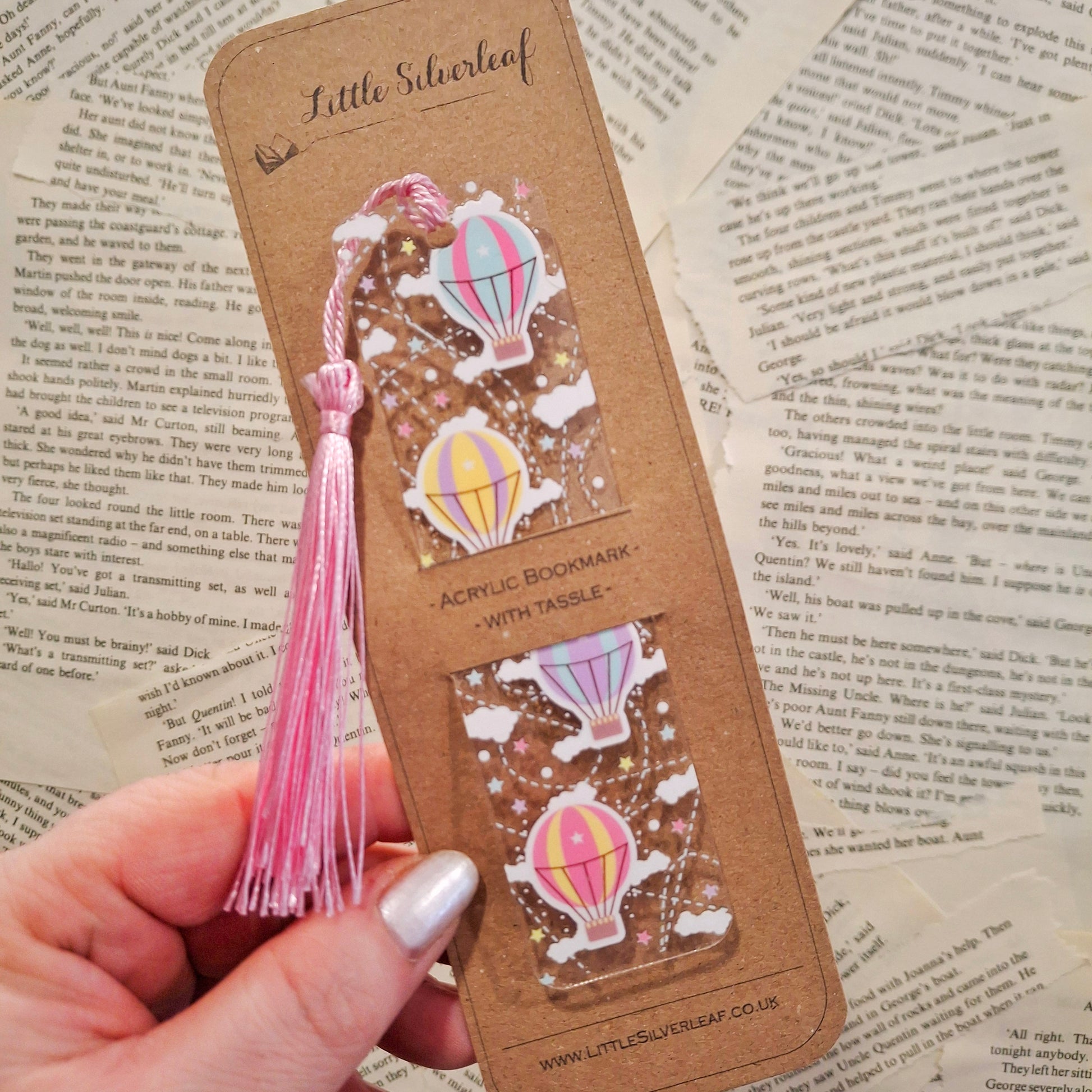 Colourful hot air balloon themed bookmark for travellers, packaged on a brown kraft backing card, held over a book page background.