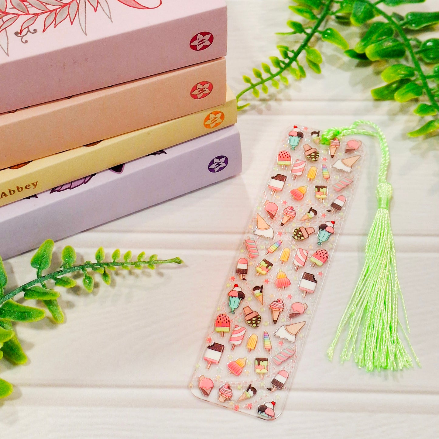 Ice cream themed acrylic bookmark with tassel on a wooden surface, with books and greenery.