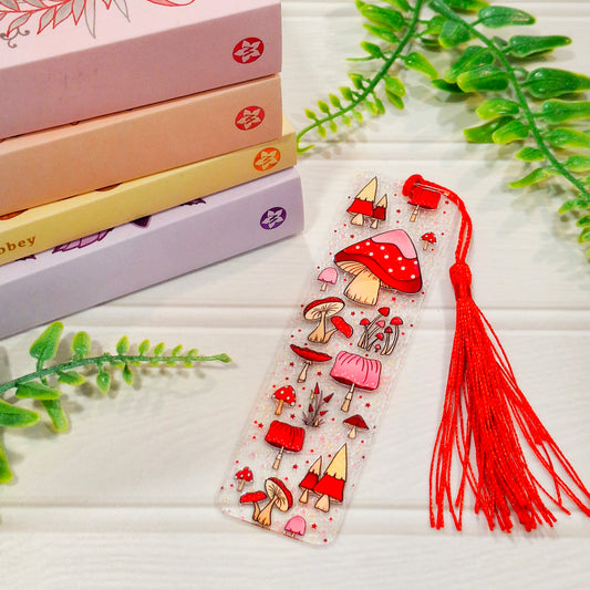 Magical mushroom acrylic bookmark with tassel on a light surface, with books and green leaves.
