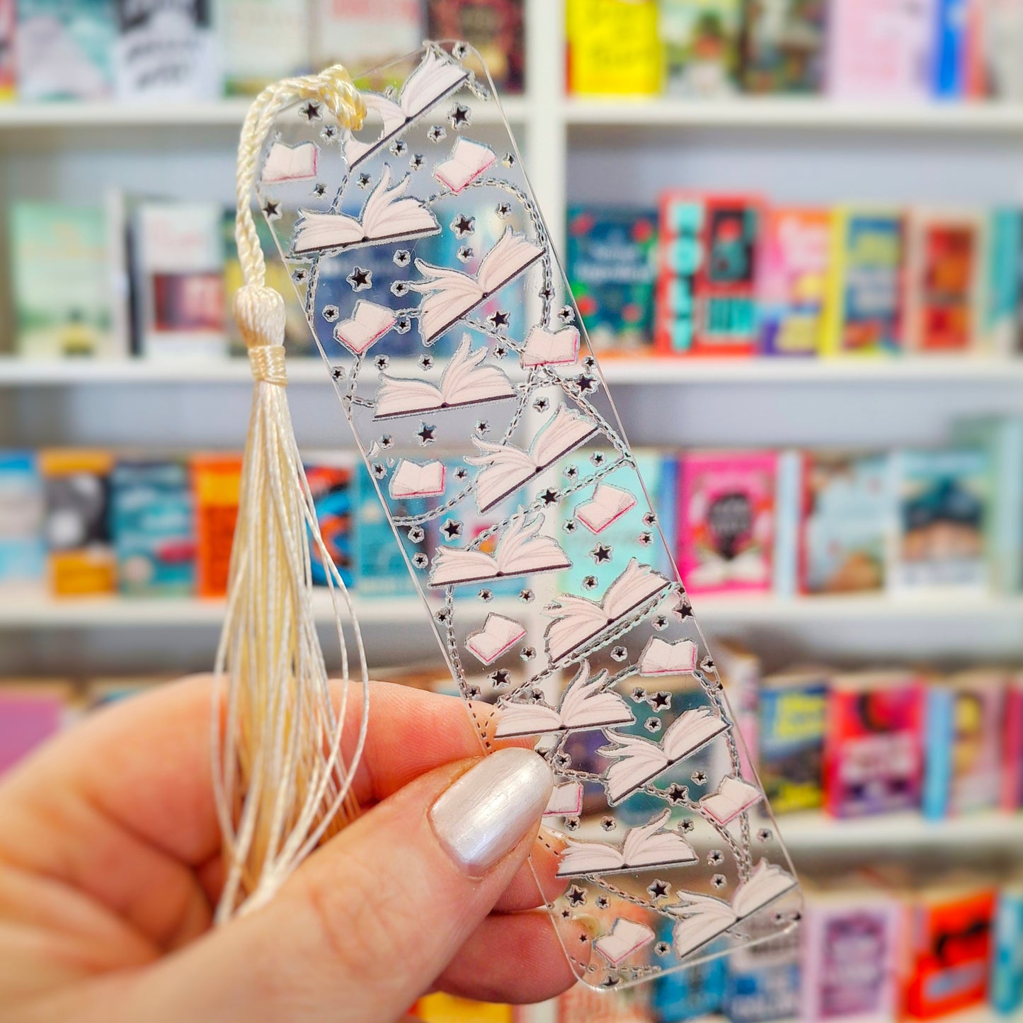 Clear paperback book pages themed bookmark with tassel held in front of a bookshelf.