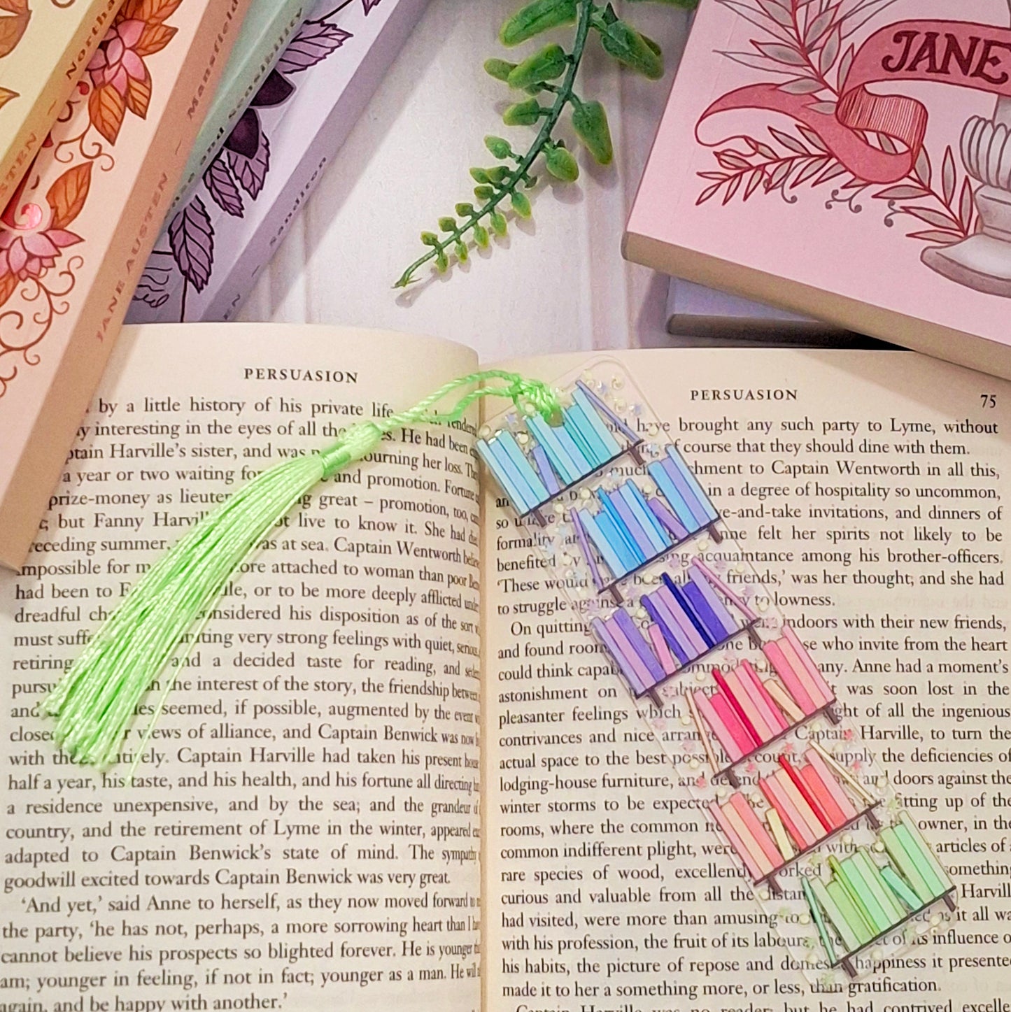 Colourful rainbow bookshelf themed bookmark with tassel for book lovers, lying across an open book page.
