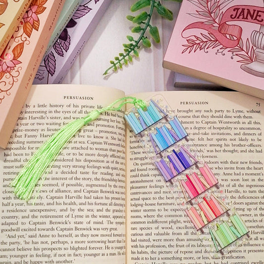 Colourful rainbow bookshelf themed bookmark with tassel for book lovers, lying across an open book page.