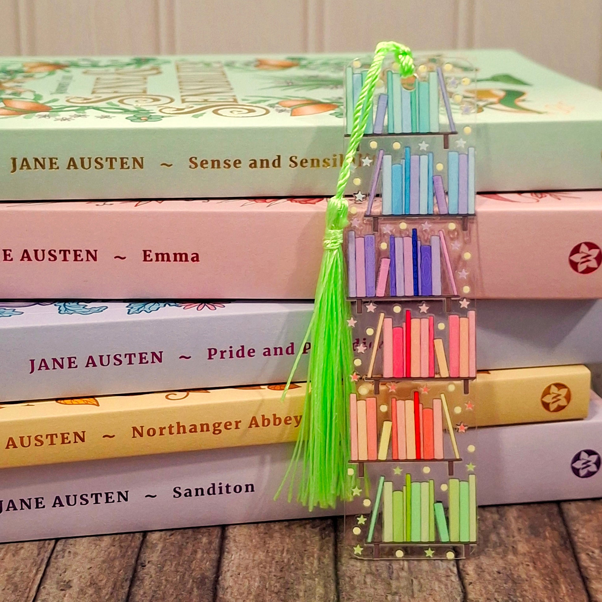 Bright rainbow library bookmark with tassel, resting against a stack of rainbow coloured books.