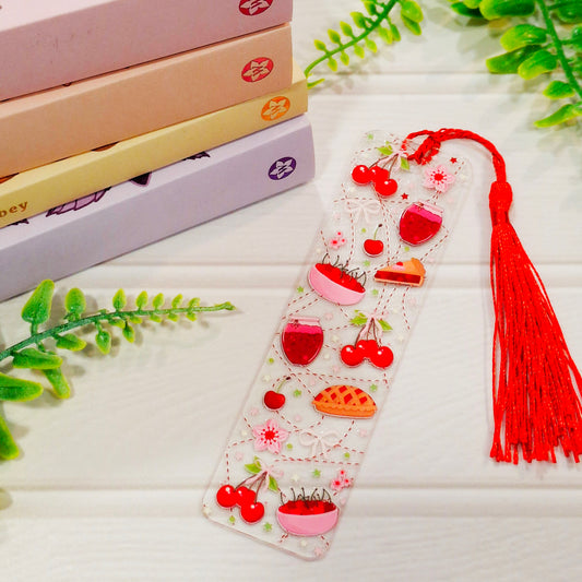 Cherry pie acrylic bookmark with retro dessert design and tassel on a light surface, with books and leaves.