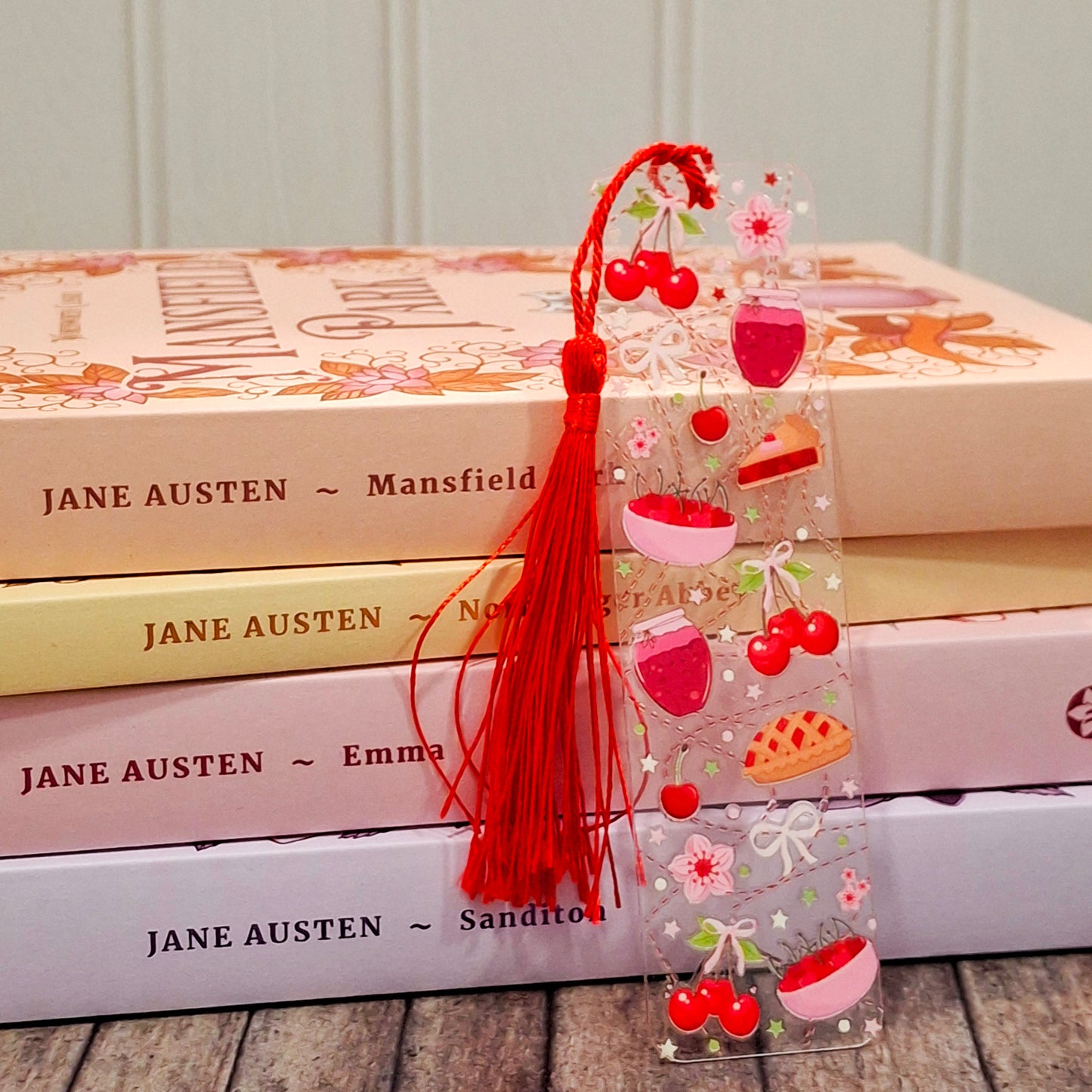 Acrylic bookmark featuring cherry pie illustrations, resting against a stack of rainbow coloured books.