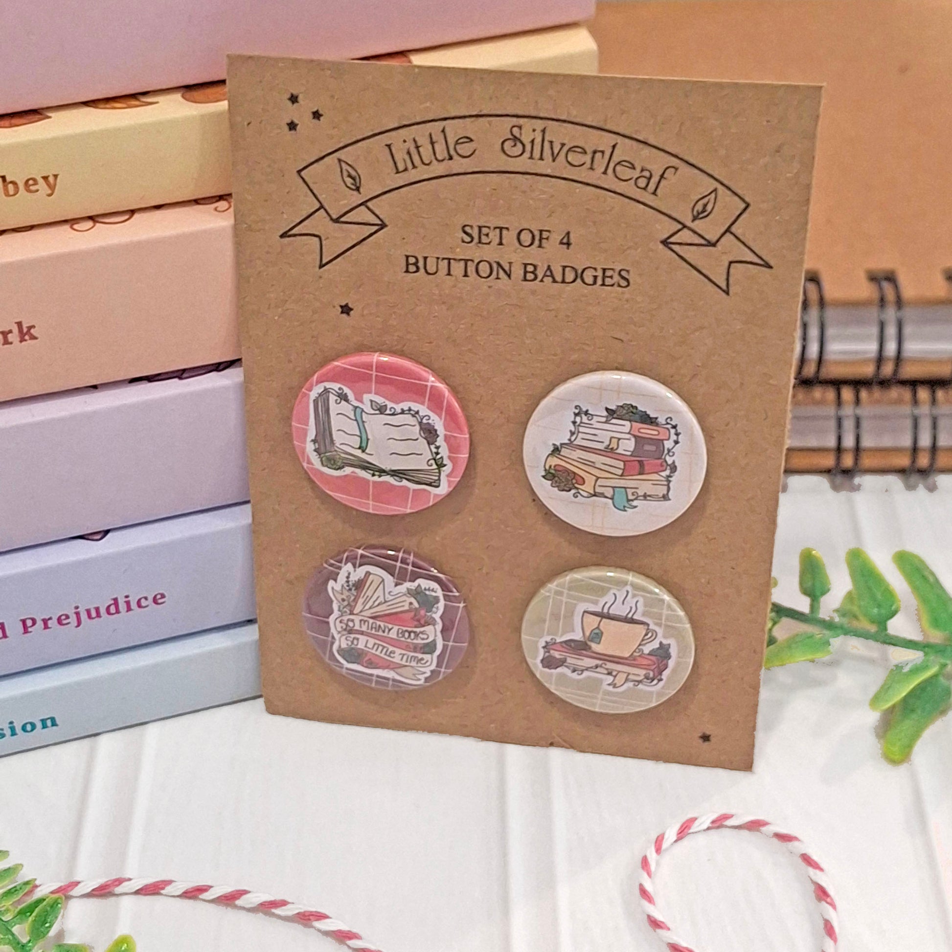 A kraft display card holding four round button badges with illustrated stationery and tea-themed designs. The card reads 'Little Silverleaf' and 'SET OF 4 BUTTON BADGES.