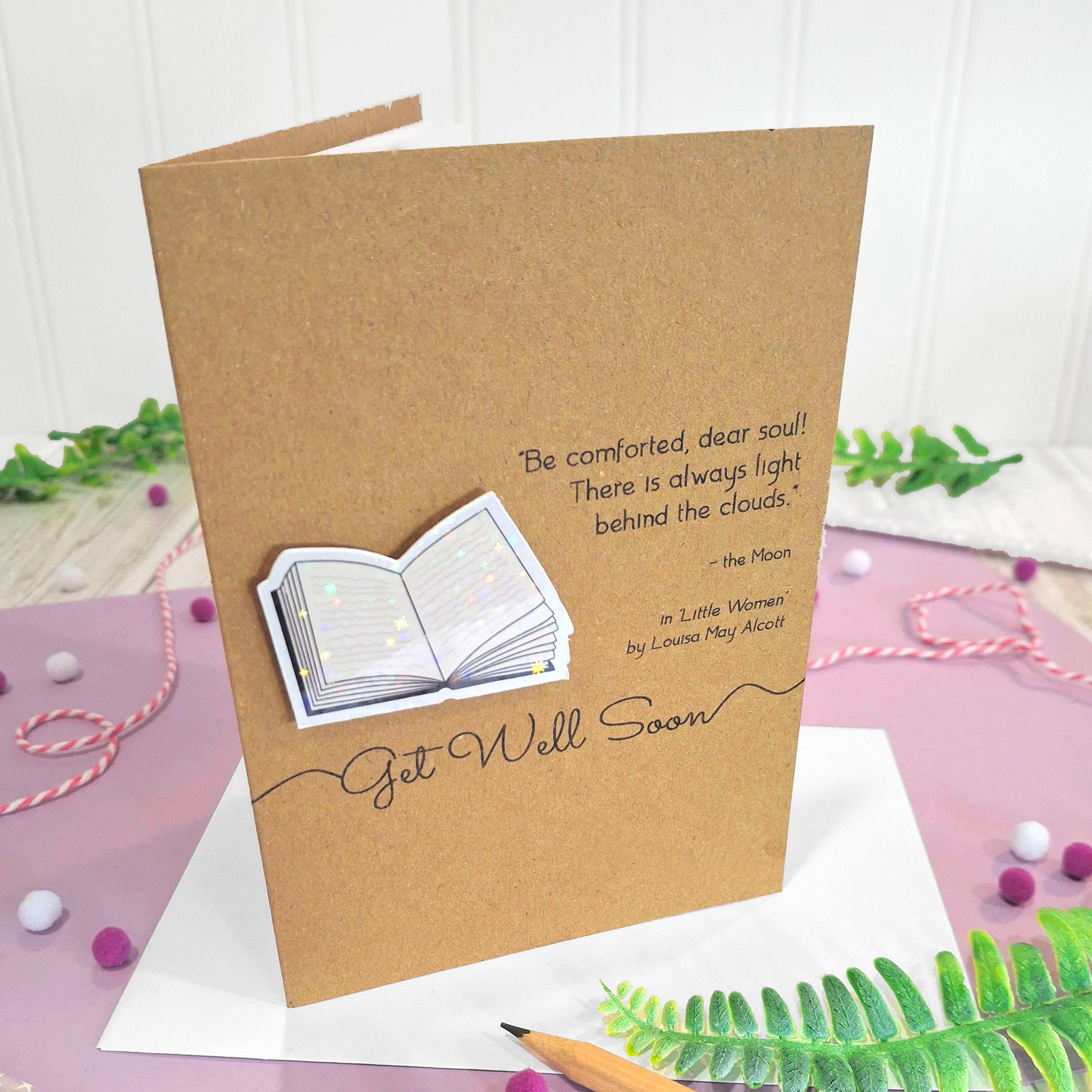 A get well card made from brown kraft card with a raised, holographic, illustrated open book embellishment, a printed quote from the book 'Little Women' by Louisa May Alcott, and the words Get well Soon.