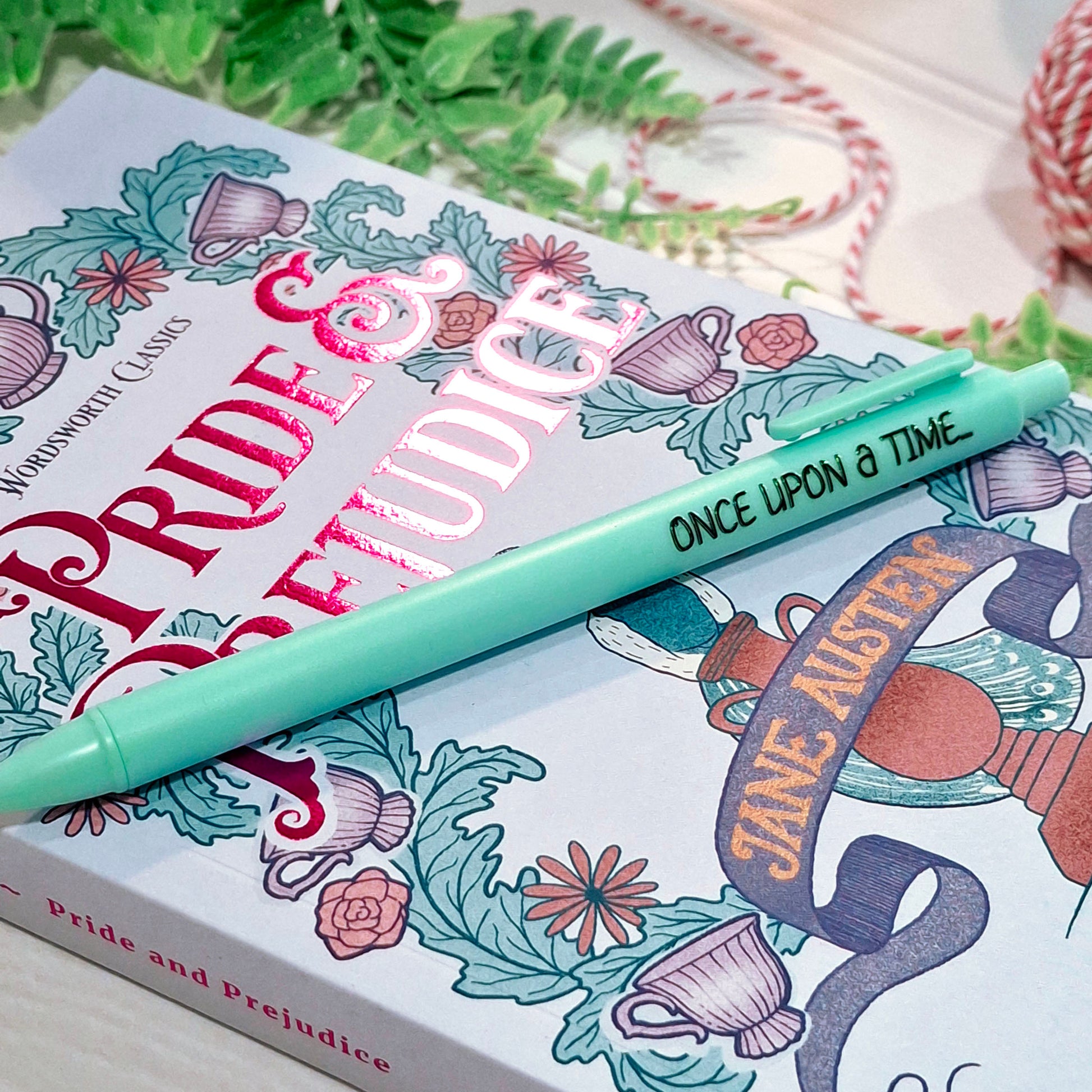 A blue pen with the printed phrase 'Once Upon a Time' resting diagonally across a book cover featuring blue and purple floral illustrations and Jane Austen-themed artwork.