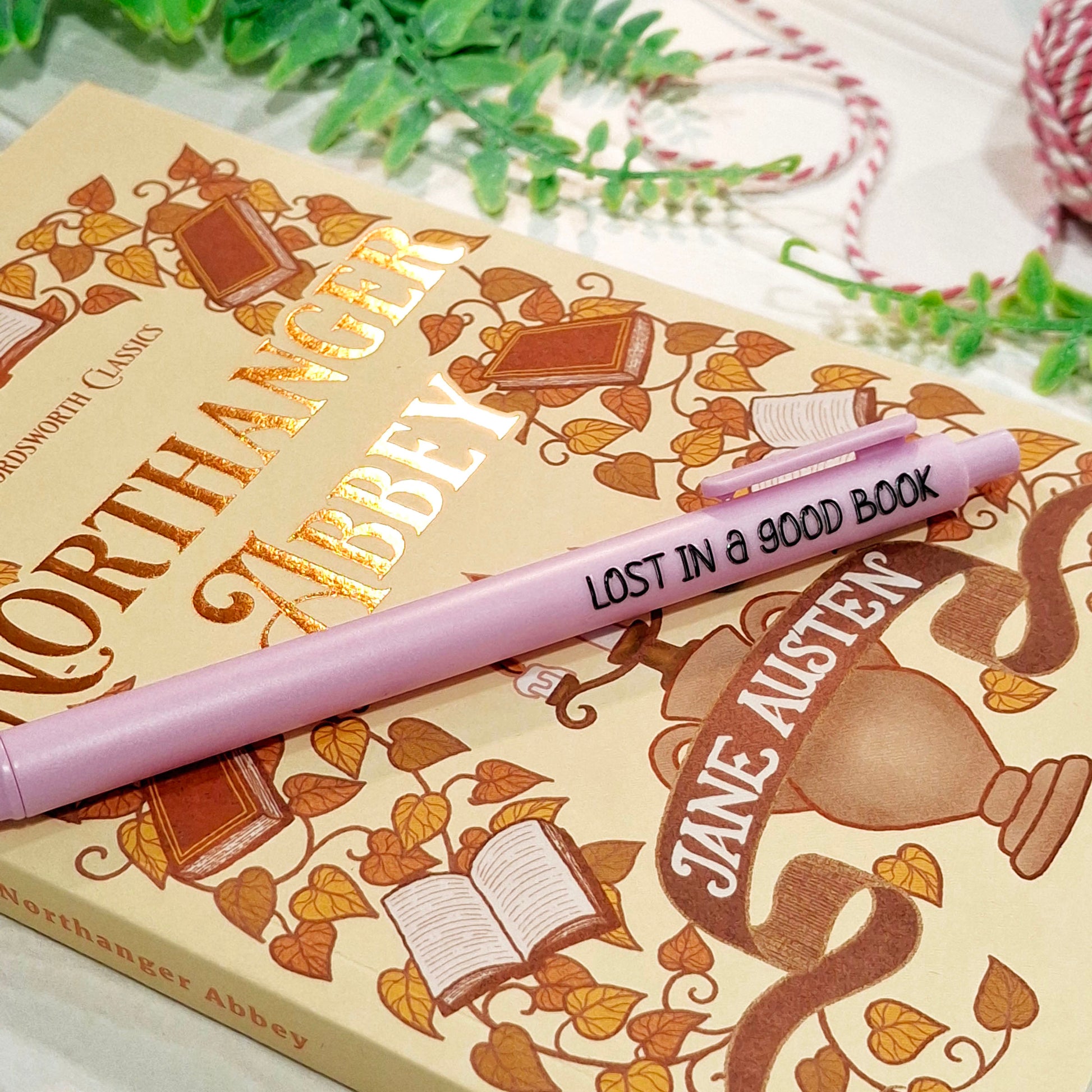 A light purple pen with black text reading 'LOST IN A GOOD BOOK' resting on a Jane Austen book cover.