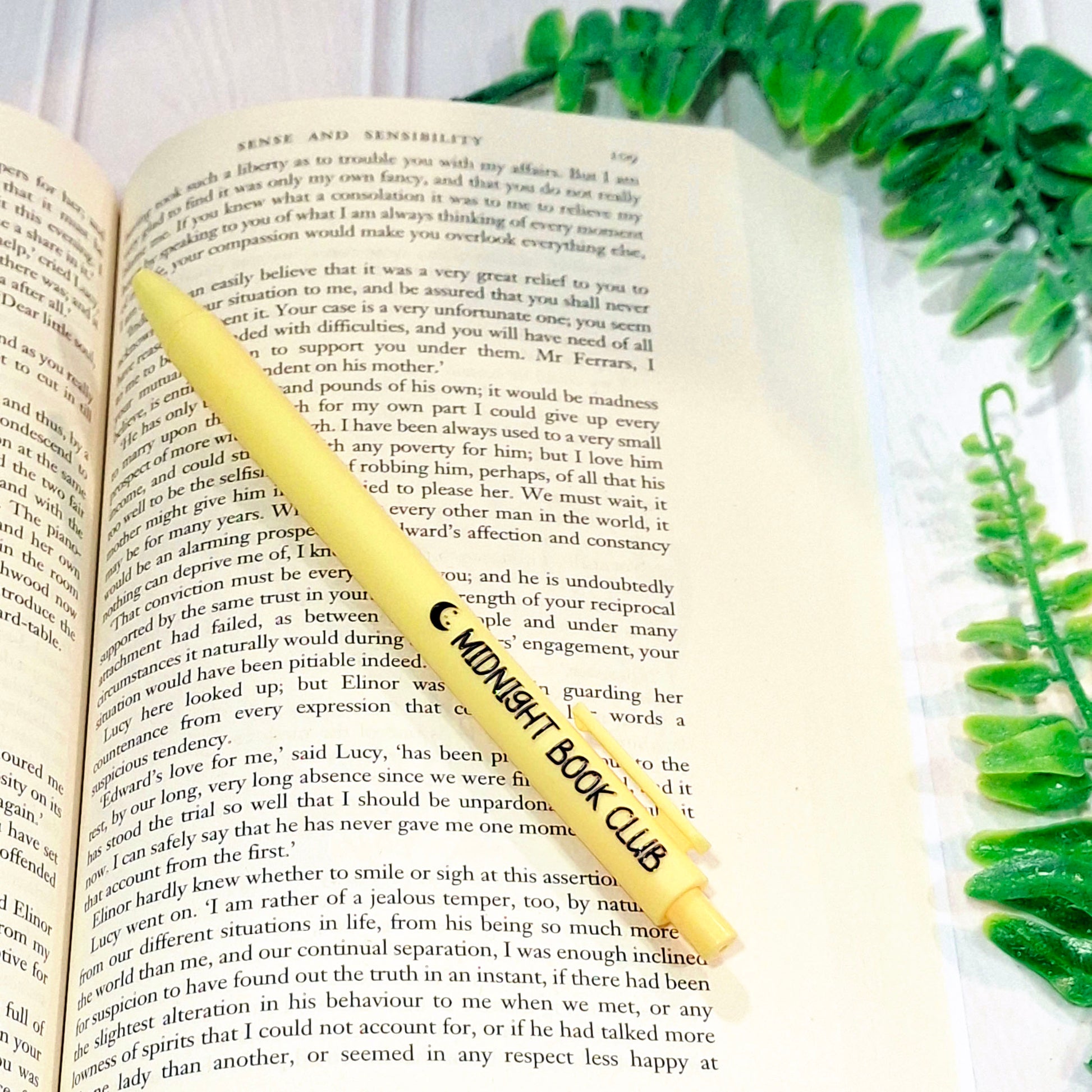 An open book with a yellow pen lying across it with the phrase 'Midnight Book Club' on it.