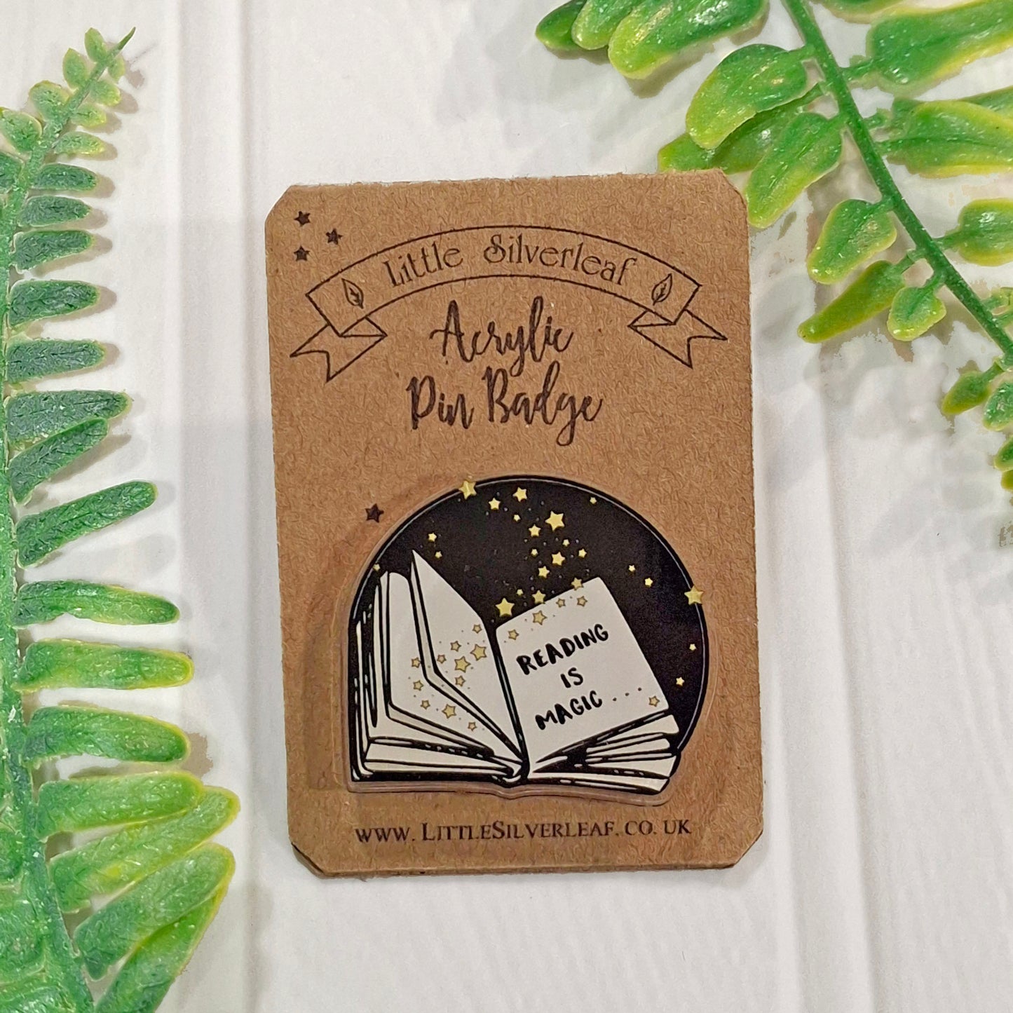 A reading-themed acrylic pin badge by Little Silverleaf, displayed on its brown kraft backing card. The badge features a black circular background with yellow stars and an open book with the words 'READING IS MAGIC' in white.