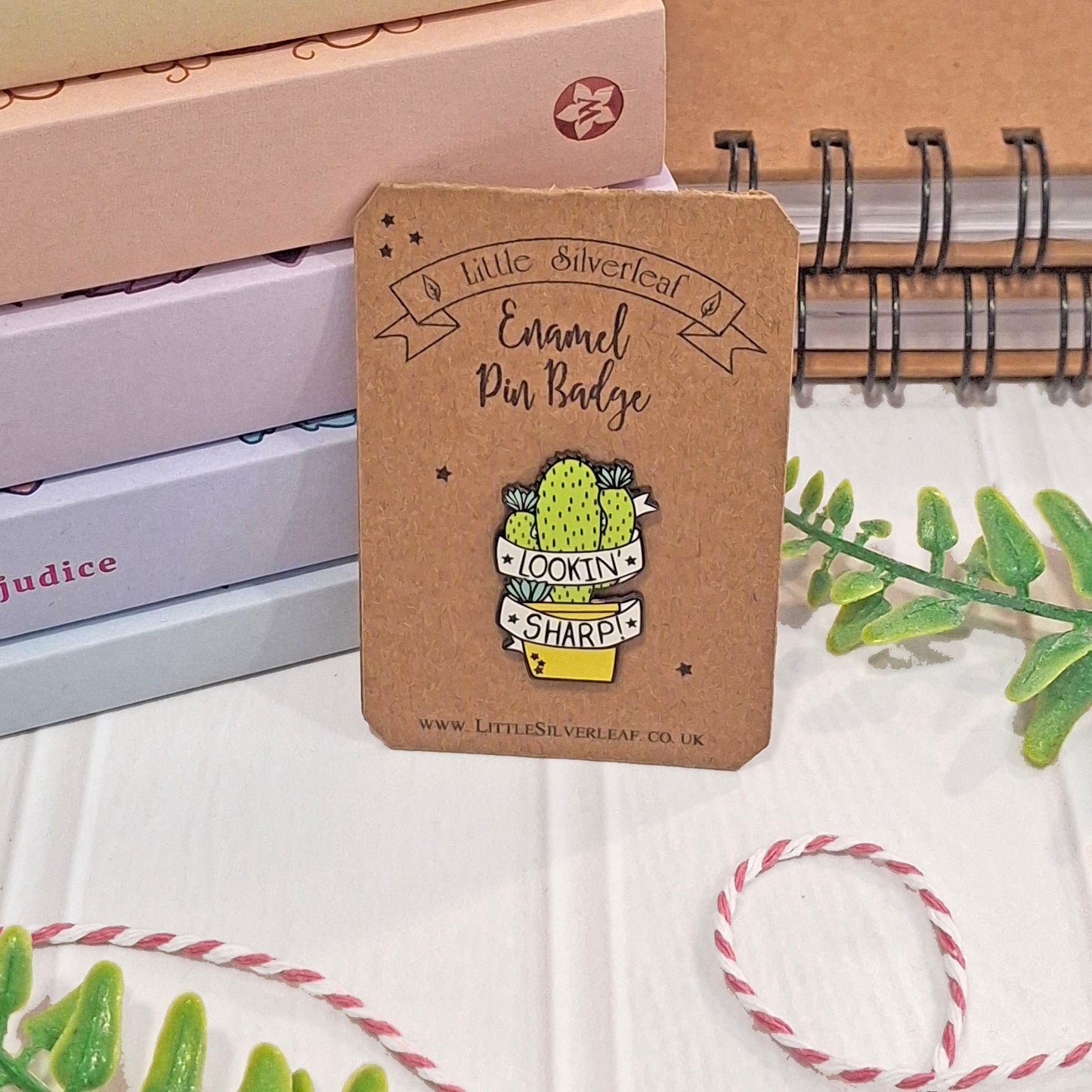 An enamel pin badge displayed on a kraft backing card. The backing card reads 'Little Silverleaf Enamel Pin Badge' and shows a cactus pin with the words 'LOOKIN' SHARP'.