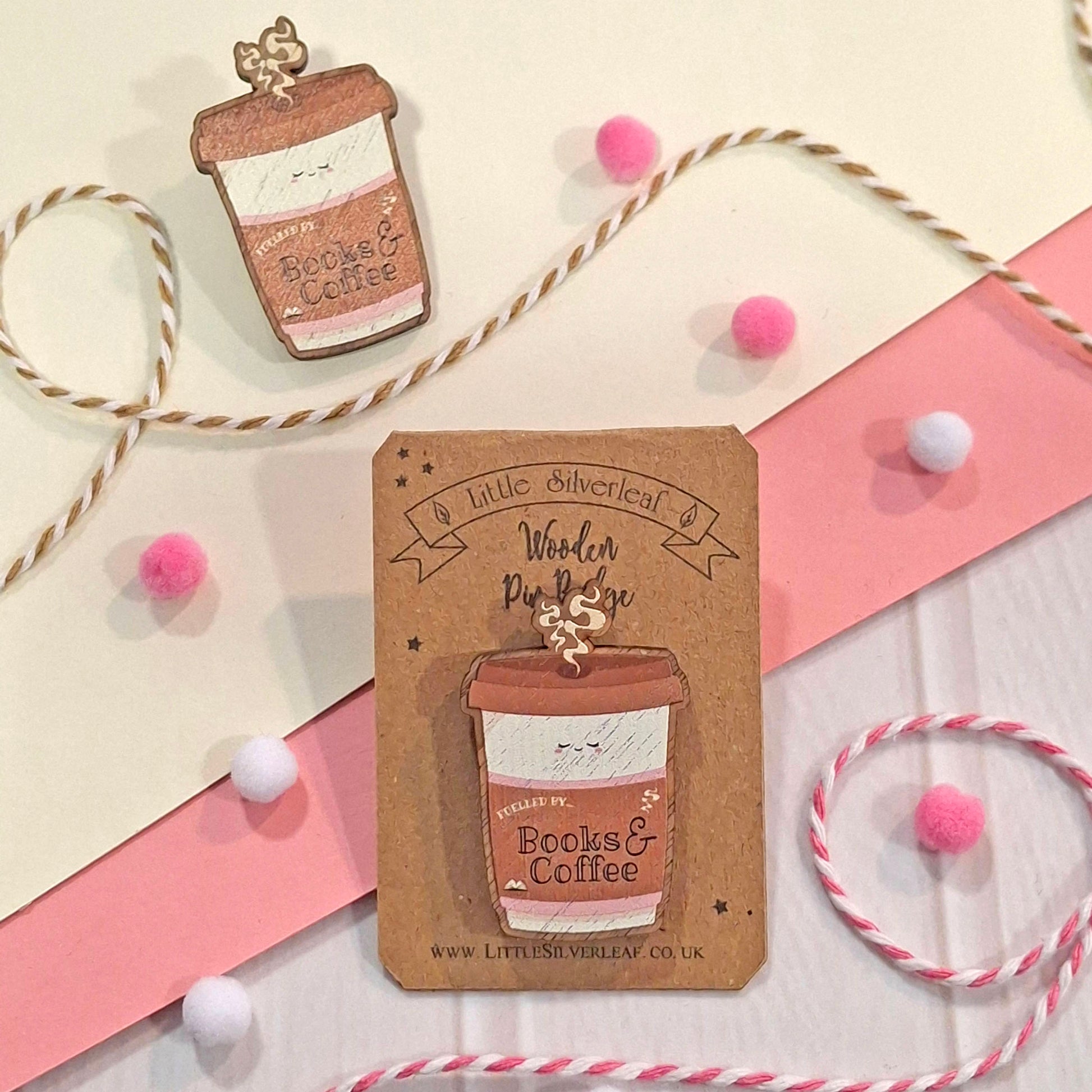 A coffee cup shaped badge attached to a kraft card that reads 'Little Silverleaf Wooden Pin Badge.' A second badge is shown above on a cream background with pink and white ribbon strips, bakers twine, and pink pom-pom accents.