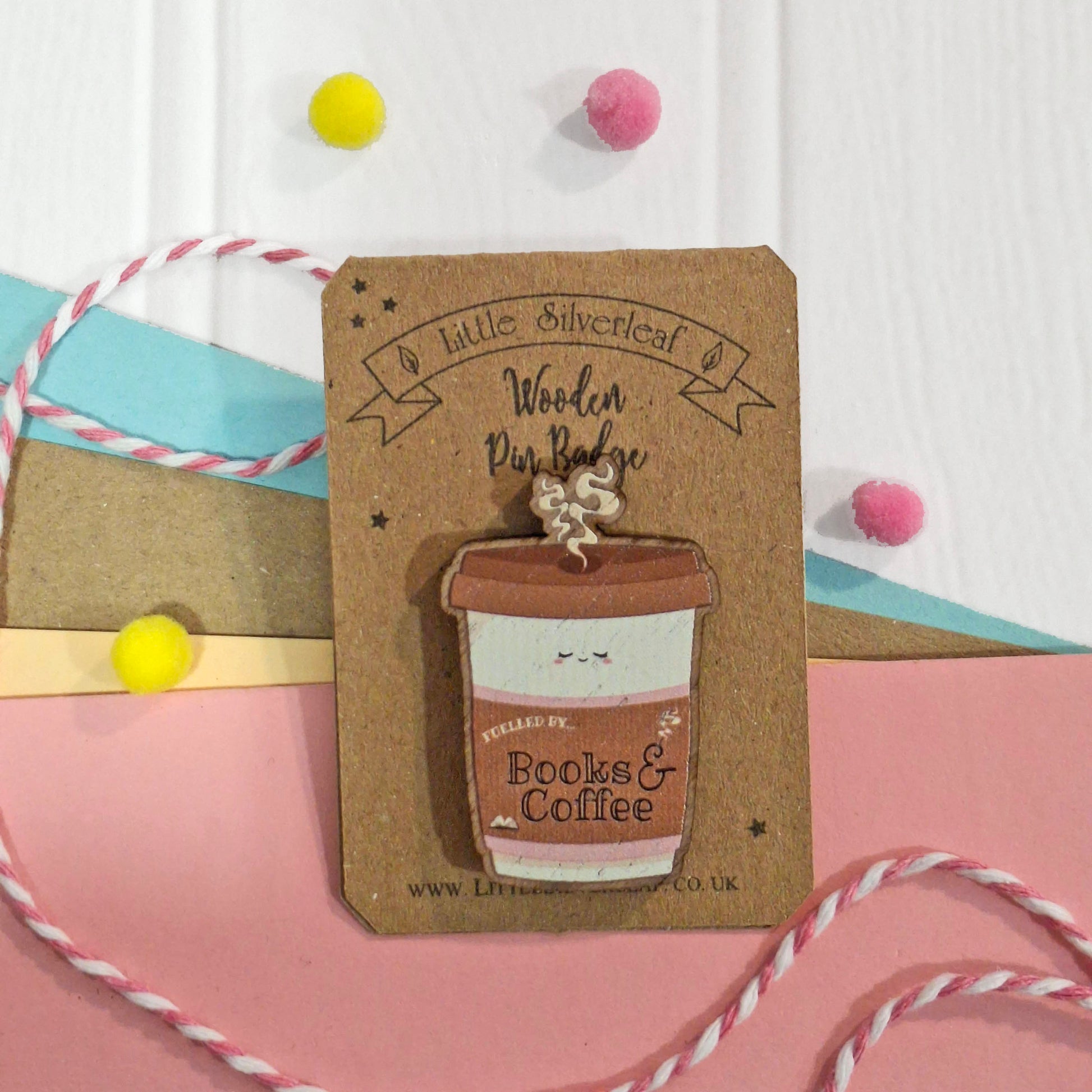 A wooden pinback badge shaped like a coffee cup, displayed on a brown kraft backing card. The badge features a light wood grain finish with a brown lid and steam rising from the top.