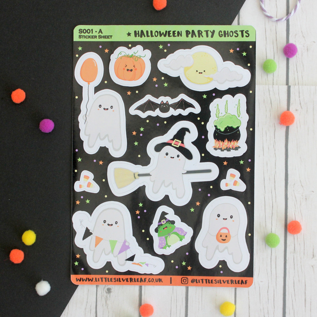 A sheet of Halloween party ghost stickers displayed on a black background with colorful pom-poms scattered around. The sticker sheet features cute cartoon ghosts, a pumpkin, a moon, a cauldron, a bat, and other spooky elements on a black background.
