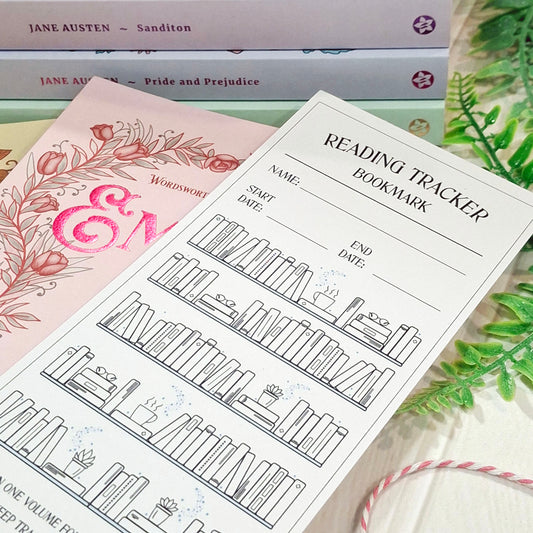 A reading tracker bookmark sheet with black line drawings of bookshelves and fill-in lines, placed over a pink floral book and stacked books in the background.