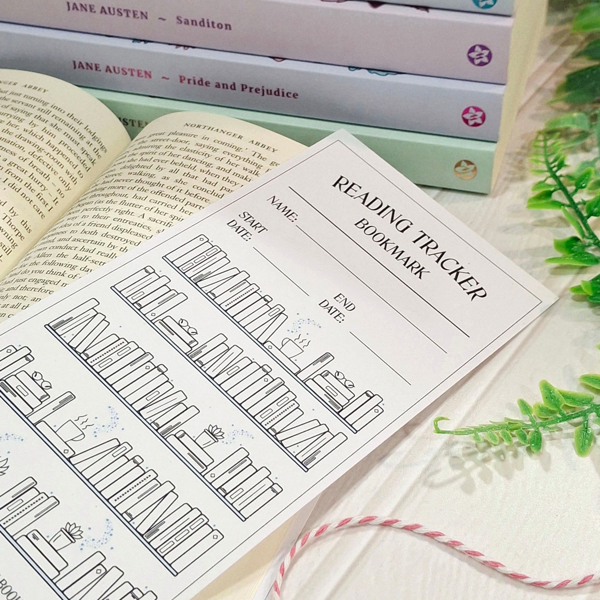 A black-and-white reading tracker bookmark sheet laid over an open book, with stacked Jane Austen books in the background and green leaves at the side.