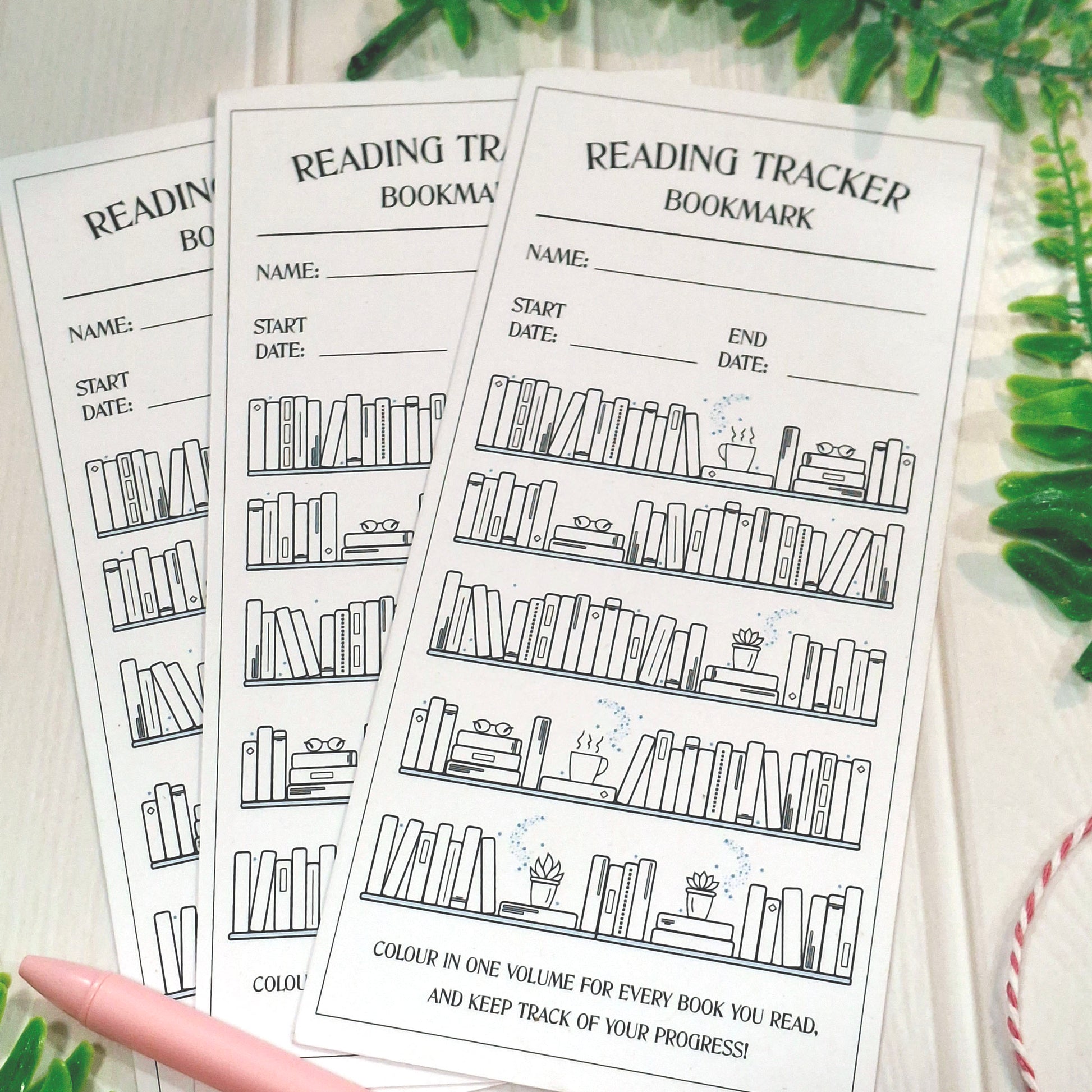 Three printable reading tracker bookmark sheets fanned out on a light surface with green leaves around the edges. The black-and-white sheets include bookshelf illustrations, fill-in lines for name and start/end dates, and text inviting users to colour in every book they read.