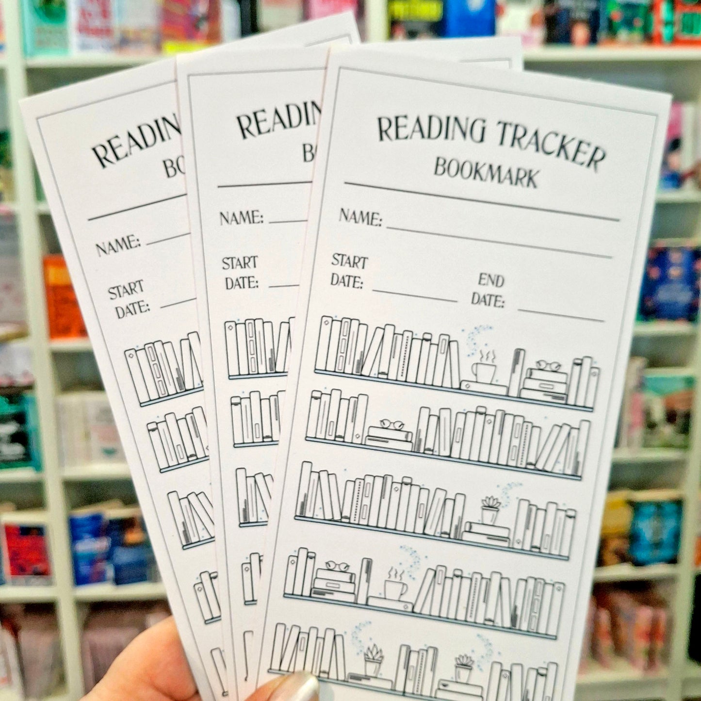 Three reading tracker bookmarks are held in a hand in front of a blurred bookstore shelf background. The bookmarks are white with black text and line drawings of bookshelves and books, with fields for name, start date, end date, and reading progress.