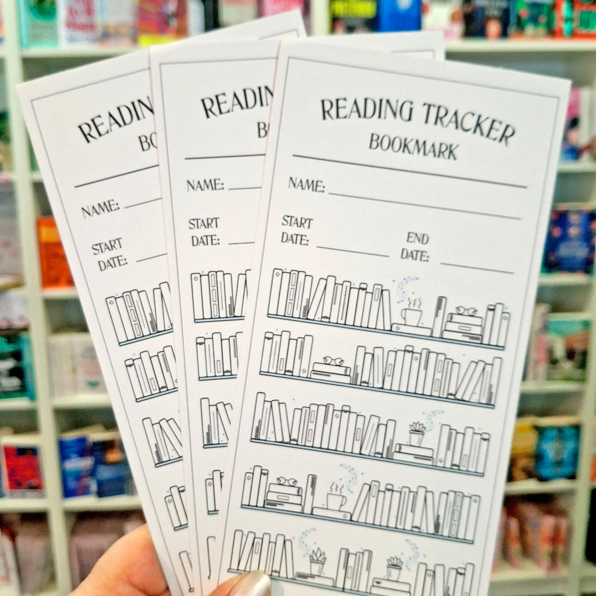 Three reading tracker bookmarks are held in a hand in front of a blurred bookstore shelf background. The bookmarks are white with black text and line drawings of bookshelves and books, with fields for name, start date, end date, and reading progress.