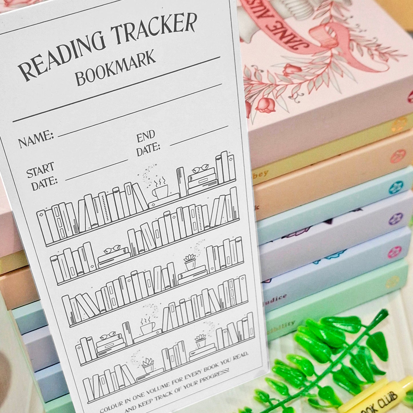A white reading tracker bookmark with black line art of bookshelves and fill-in lines for name, start date, and end date, displayed in front of a stack of pastel-colored books.