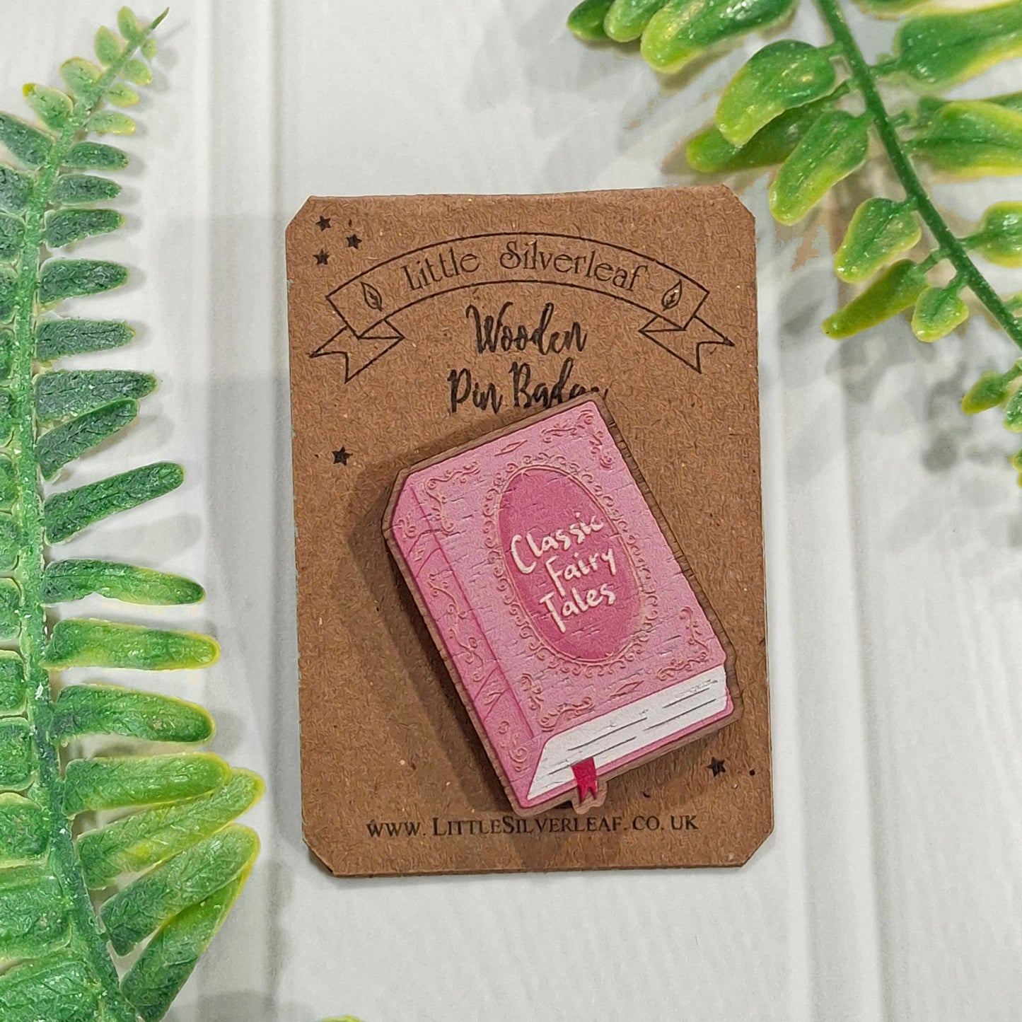 A small pink wooden book pin badge with the words 'Classic Fairy Tales' on its cover, mounted on a brown cardboard backing card. The backing card has the brand name 'Little Silverleaf' printed on it.