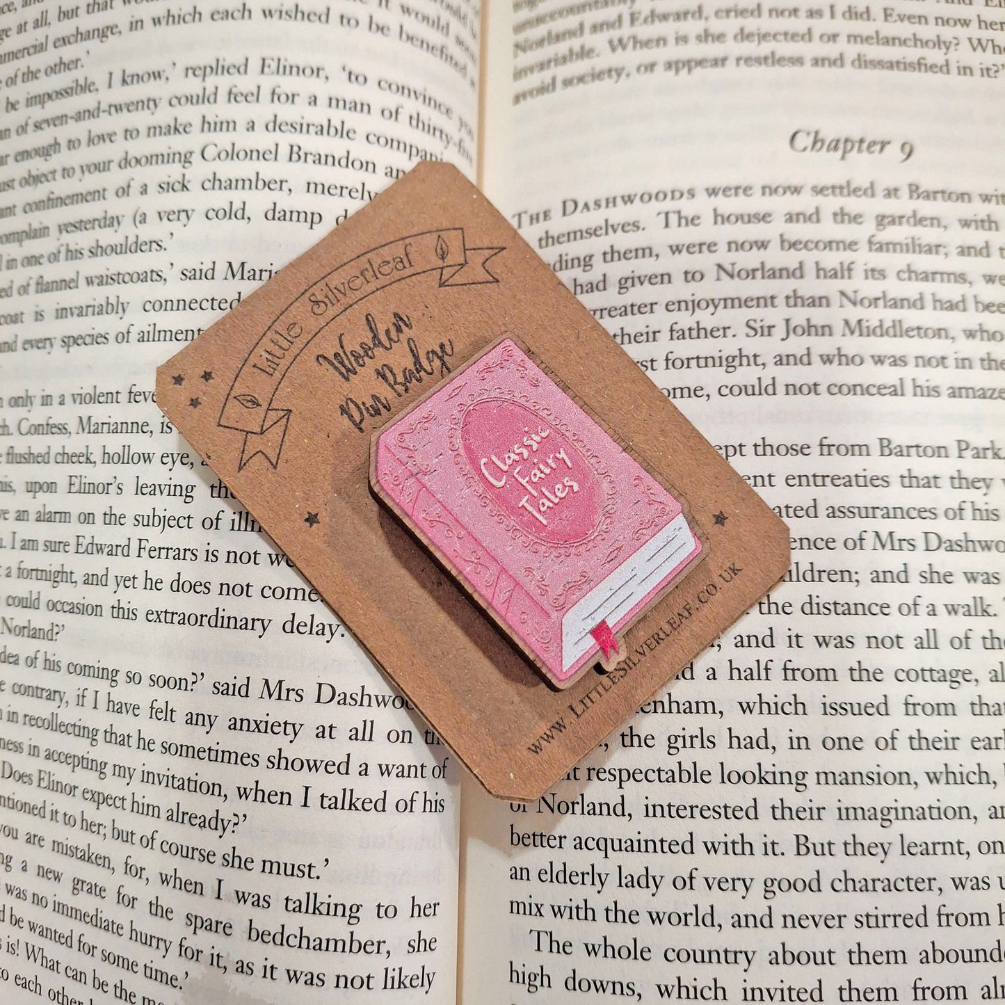 A decorative wooden book pin badge shaped placed on an open book page. The badge reads 'Classic Fairy Tales'.